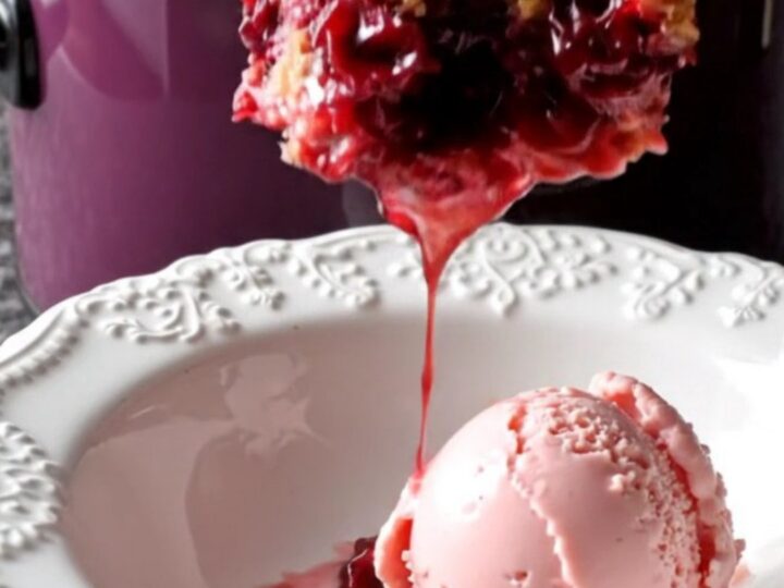 A dark plum ceramic slow cooker filled with a bubbling cherry crisp topped with a golden almond crumble.