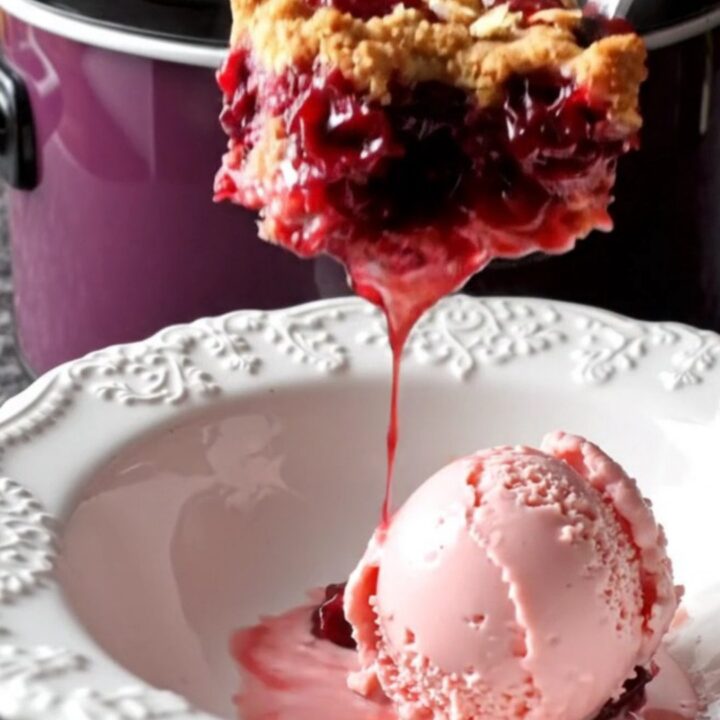 A dark plum ceramic slow cooker filled with a bubbling cherry crisp topped with a golden almond crumble.