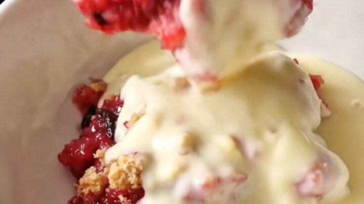 A close-up of a spoon lifting a scoop of strawberry rhubarb crumble from a mint-colored slow cooker.