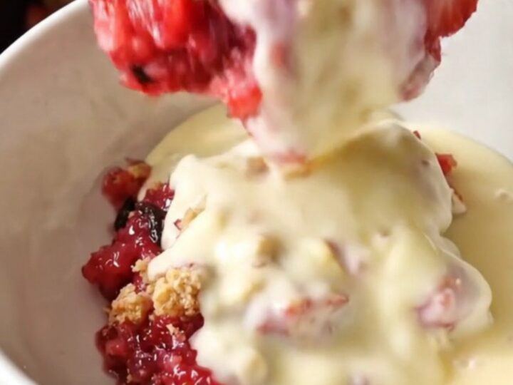 A close-up of a spoon lifting a scoop of strawberry rhubarb crumble from a mint-colored slow cooker.