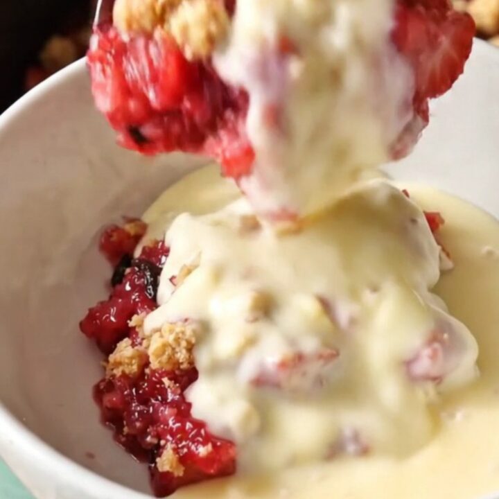 A close-up of a spoon lifting a scoop of strawberry rhubarb crumble from a mint-colored slow cooker.