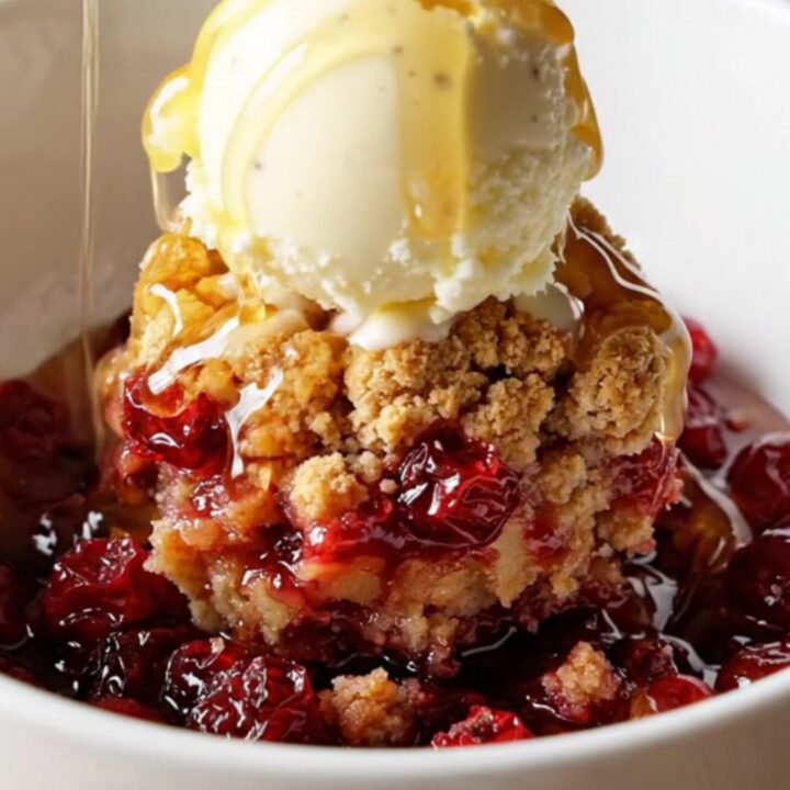 A close-up of a deep green slow cooker filled with a bubbling cranberry apple crumble topped with golden oats and walnuts.