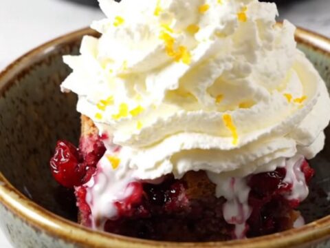 A rustic ruby-red stoneware crockpot filled with a vibrant blood orange and cranberry cobbler topped with a golden pecan