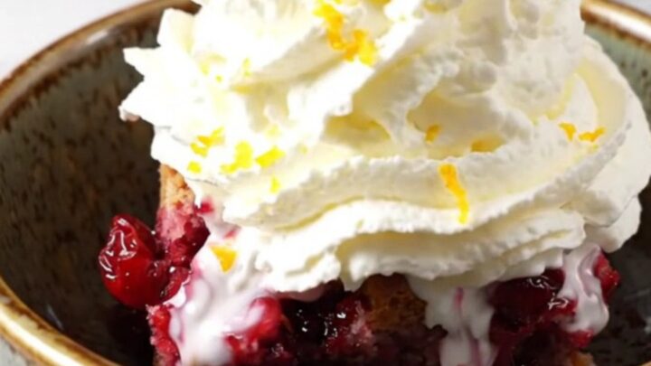 A rustic ruby-red stoneware crockpot filled with a vibrant blood orange and cranberry cobbler topped with a golden pecan
