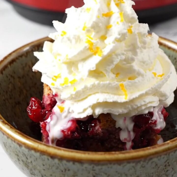A rustic ruby-red stoneware crockpot filled with a vibrant blood orange and cranberry cobbler topped with a golden pecan