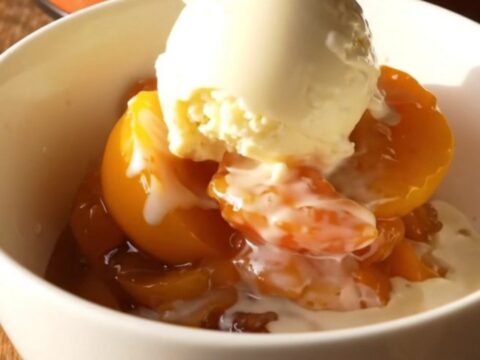 A warm, bubbling nectarine cobbler in a terracotta slow cooker with golden biscuit topping.