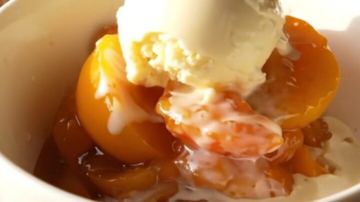 A warm, bubbling nectarine cobbler in a terracotta slow cooker with golden biscuit topping.