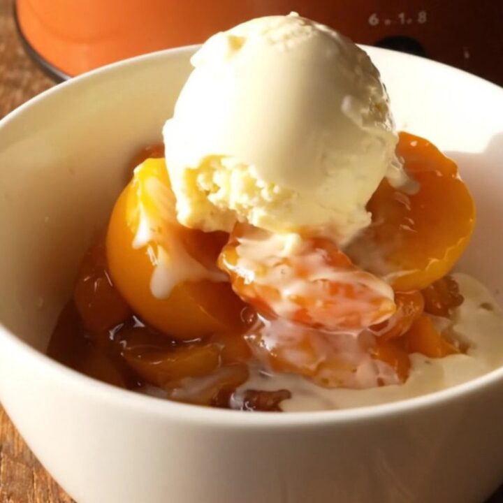 A warm, bubbling nectarine cobbler in a terracotta slow cooker with golden biscuit topping.