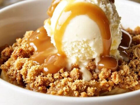 A warm, bubbling bowl of caramel banana crisp topped with golden roasted macadamia nuts and oats