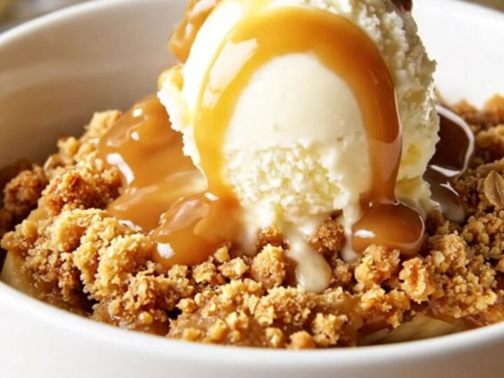 A warm, bubbling bowl of caramel banana crisp topped with golden roasted macadamia nuts and oats