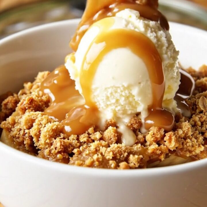 A warm, bubbling bowl of caramel banana crisp topped with golden roasted macadamia nuts and oats