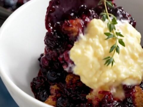 A rustic navy-blue crockpot filled with bubbly wild blueberry cobbler topped with golden cornmeal biscuits.