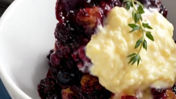 A rustic navy-blue crockpot filled with bubbly wild blueberry cobbler topped with golden cornmeal biscuits.