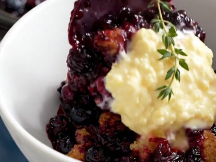 A rustic navy-blue crockpot filled with bubbly wild blueberry cobbler topped with golden cornmeal biscuits.