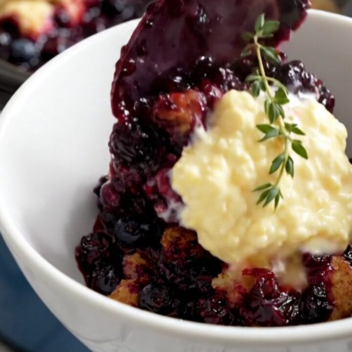 A rustic navy-blue crockpot filled with bubbly wild blueberry cobbler topped with golden cornmeal biscuits.
