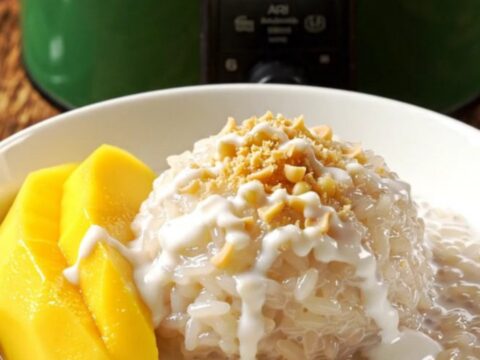 A jade-green crockpot filled with creamy Thai mango sticky rice topped with fresh yellow mango slices.