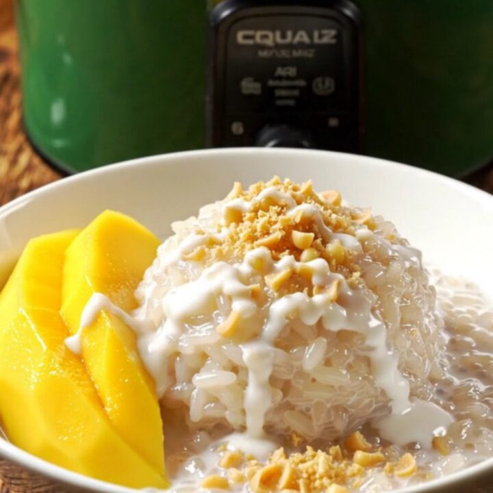 A jade-green crockpot filled with creamy Thai mango sticky rice topped with fresh yellow mango slices.