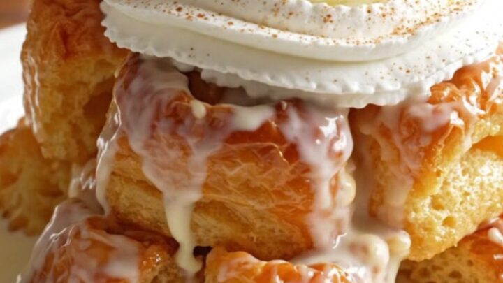 A warm, golden serving of tres leches brioche bread pudding topped with whipped cream and a cherry in a shallow bowl.
