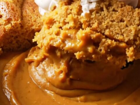 A warm, creamy pumpkin pudding cake in a stoneware slow cooker with a spoon lifting a portion.