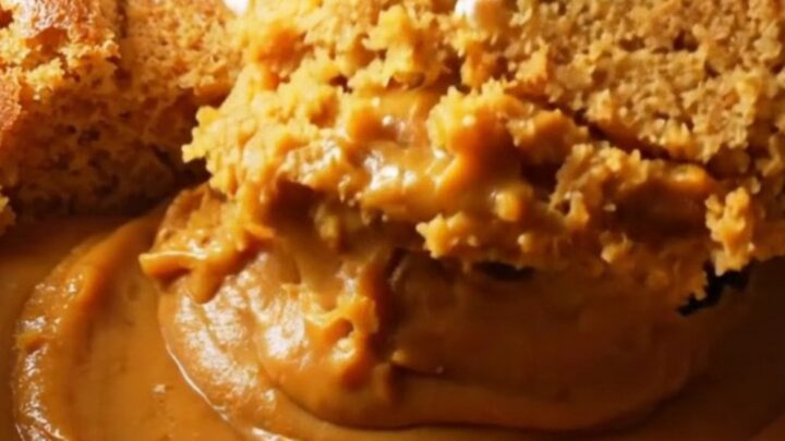 A warm, creamy pumpkin pudding cake in a stoneware slow cooker with a spoon lifting a portion.