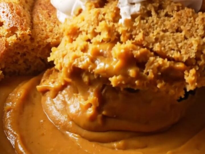 A warm, creamy pumpkin pudding cake in a stoneware slow cooker with a spoon lifting a portion.