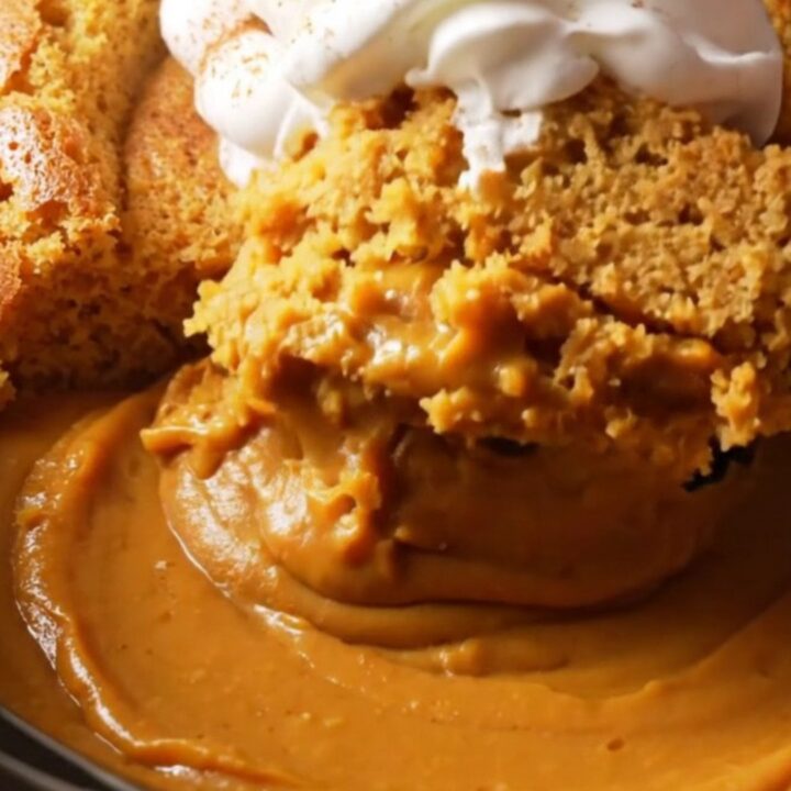 A warm, creamy pumpkin pudding cake in a stoneware slow cooker with a spoon lifting a portion.