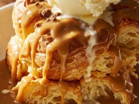 A close-up of a slow cooker filled with golden, custard-soaked brioche bread pudding, topped with cookie crumbs.
