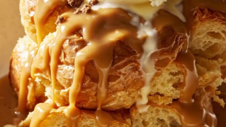 A close-up of a slow cooker filled with golden, custard-soaked brioche bread pudding, topped with cookie crumbs.