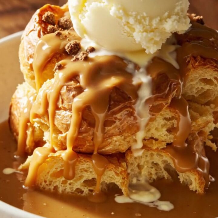 A close-up of a slow cooker filled with golden, custard-soaked brioche bread pudding, topped with cookie crumbs.
