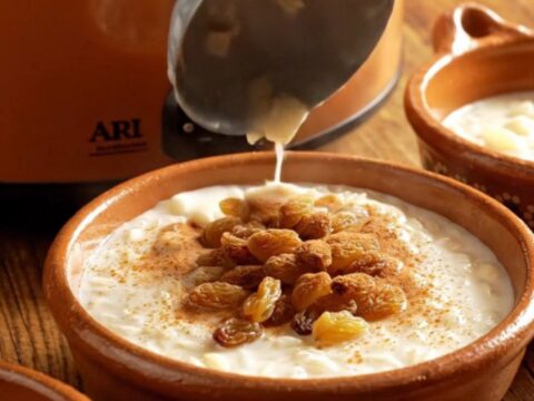 A close-up view of creamy Arroz con Leche in a rustic clay bowl topped with a dusting of cinnamon and golden raisins.