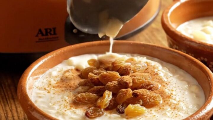 A close-up view of creamy Arroz con Leche in a rustic clay bowl topped with a dusting of cinnamon and golden raisins.