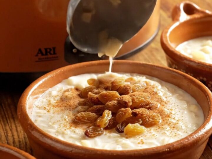 A close-up view of creamy Arroz con Leche in a rustic clay bowl topped with a dusting of cinnamon and golden raisins.
