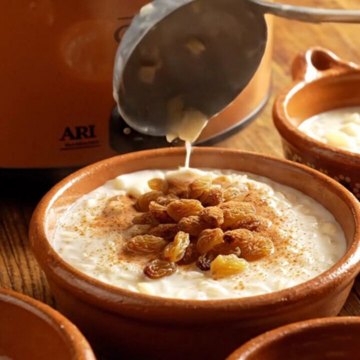 A close-up view of creamy Arroz con Leche in a rustic clay bowl topped with a dusting of cinnamon and golden raisins.
