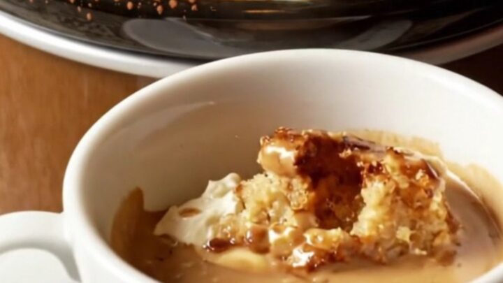A warm, creamy tiramisu brioche bread pudding in a mocha-brown ceramic crockpot, dusted with cocoa powder.