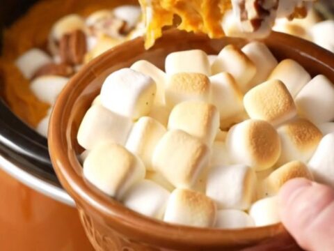 A close-up of a slow cooker filled with creamy sweet potato casserole topped with toasted marshmallows and pecans.