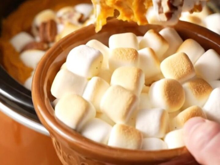 A close-up of a slow cooker filled with creamy sweet potato casserole topped with toasted marshmallows and pecans.