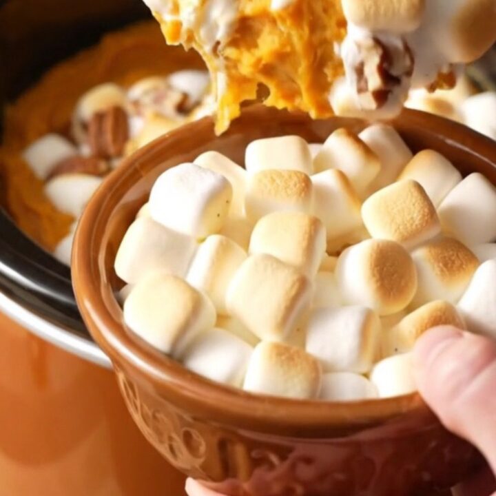 A close-up of a slow cooker filled with creamy sweet potato casserole topped with toasted marshmallows and pecans.