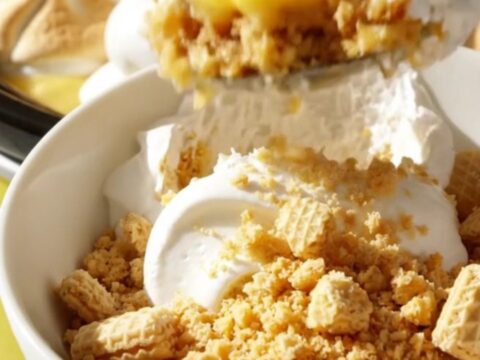 A pastel yellow ceramic slow cooker filled with a layered lemon meringue pudding, topped with soft marshmallow peaks.