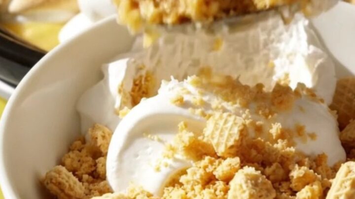 A pastel yellow ceramic slow cooker filled with a layered lemon meringue pudding, topped with soft marshmallow peaks.