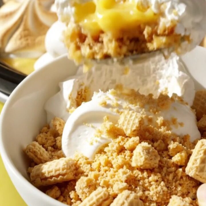 A pastel yellow ceramic slow cooker filled with a layered lemon meringue pudding, topped with soft marshmallow peaks.
