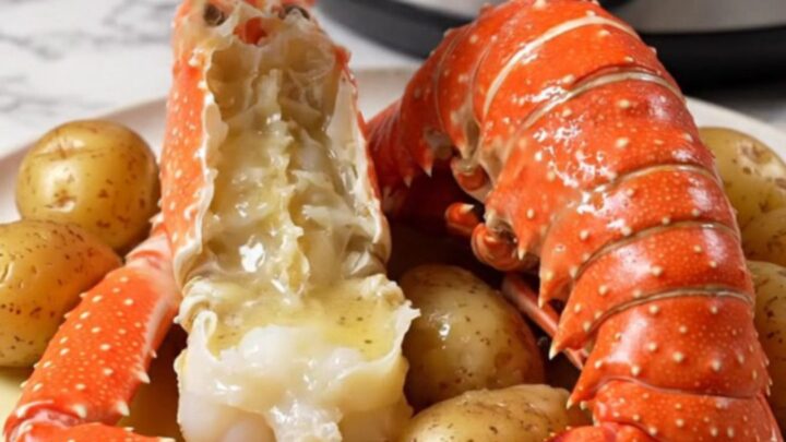 A close-up of split Alaskan king crab legs and lobster tails in a ceramic slow cooker with garlic butter.