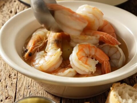 A steaming bowl of Lowcountry Frogmore stew featuring jumbo shrimp, kielbasa, and corn, served in a rustic kitchen setting.