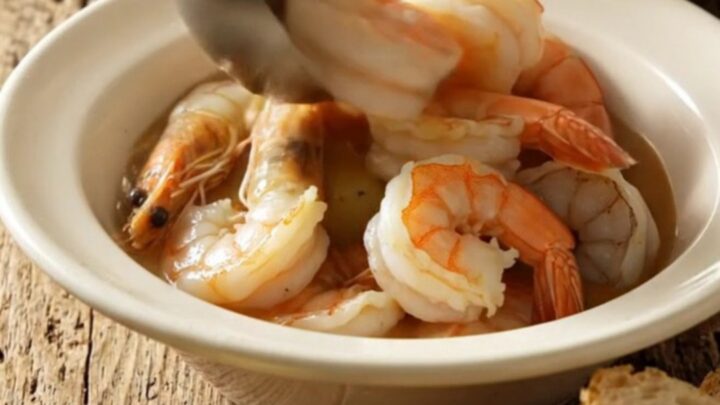 A steaming bowl of Lowcountry Frogmore stew featuring jumbo shrimp, kielbasa, and corn, served in a rustic kitchen setting.