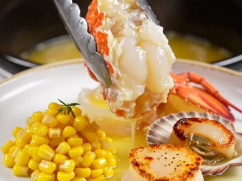 A close-up of butter-poached Maine lobster tails and sea scallops served on a warm plate with sweet corn.