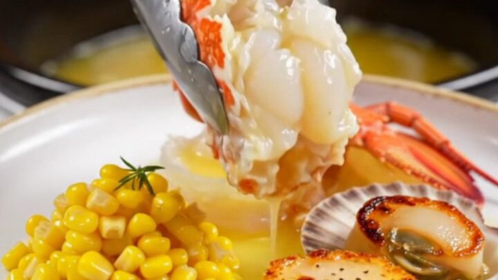 A close-up of butter-poached Maine lobster tails and sea scallops served on a warm plate with sweet corn.
