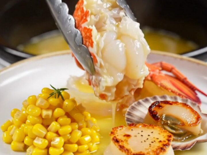 A close-up of butter-poached Maine lobster tails and sea scallops served on a warm plate with sweet corn.