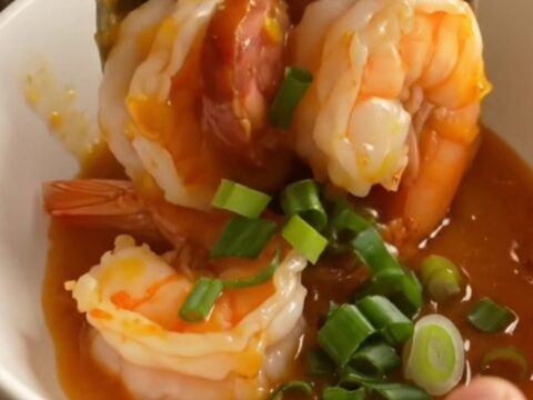 A ceramic Crockpot filled with jumbo shrimp, chorizo coins, soft-boiled eggs, and potatoes in a glossy honey-hot Cajun glaze.