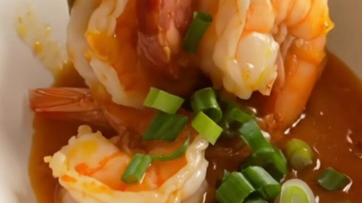 A ceramic Crockpot filled with jumbo shrimp, chorizo coins, soft-boiled eggs, and potatoes in a glossy honey-hot Cajun glaze.