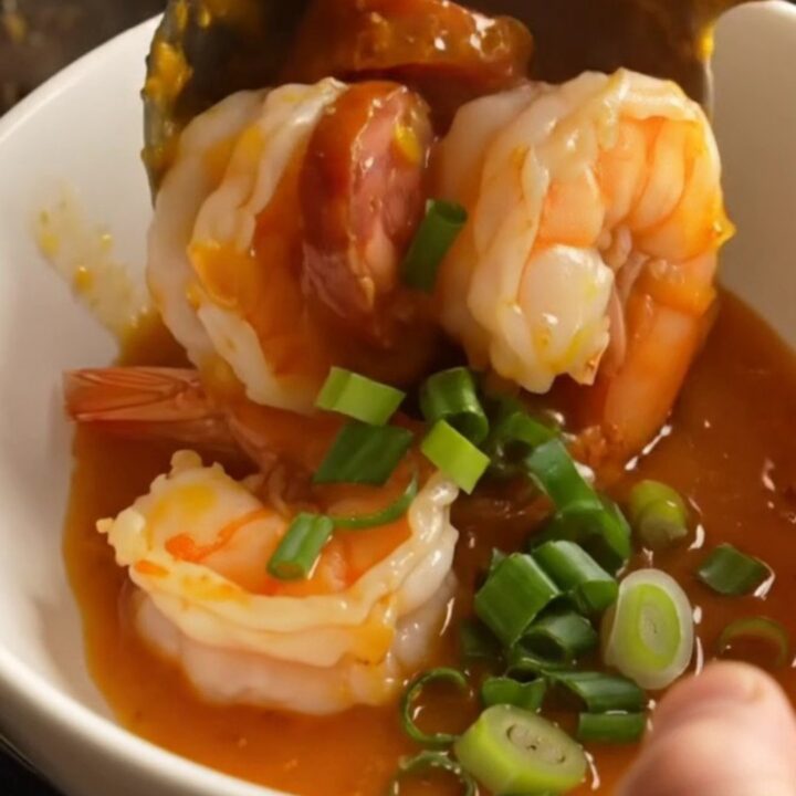 A ceramic Crockpot filled with jumbo shrimp, chorizo coins, soft-boiled eggs, and potatoes in a glossy honey-hot Cajun glaze.