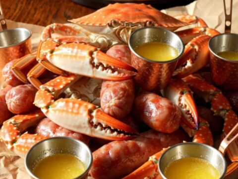 A close-up of a steaming Crockpot filled with blue crab claws, smoked sausage, and corn in a spiced Old Bay broth.